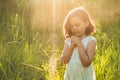 Little Girl closed her eyes, praying in a field during beautiful sunset. Hands folded in prayer concept for faith