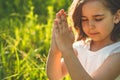 Little Girl closed her eyes, praying in a field during beautiful sunset. Hands folded in prayer concept for faith Royalty Free Stock Photo