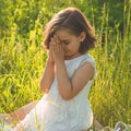 Little Girl closed her eyes, praying in a field during beautiful sunset. Hands folded in prayer concept for faith Royalty Free Stock Photo