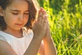 Little Girl closed her eyes, praying in a field during beautiful sunset. Hands folded in prayer concept for faith Royalty Free Stock Photo