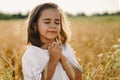 Little Girl closed her eyes, praying in a field wheat. Hands folded in prayer.