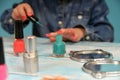 A little girl clumsily paints her nails with red varnish. Lipstick, mirror and other cosmetics are on the table