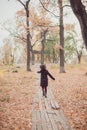 Little girl in a coat running away the road in the autumn park.