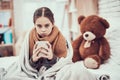 Little girl with cold in scarf and blanket with hot beverage in hands at home.