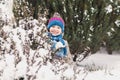 A little girl in a colored hat looks out from behind a snow-covered bush. Royalty Free Stock Photo