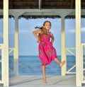 Little girl in colorful dress jumping and dancing on the white wooden pier near the ocean.