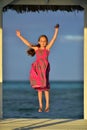 Little girl in colorful dress jumping and dancing on the white wooden pier near the ocean. Royalty Free Stock Photo