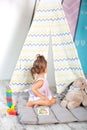 Little girl in colorful wigwam with toys. child plays with colorful toy blocks. Developing and creative toys and games for young c Royalty Free Stock Photo