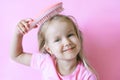 Little girl combing her hair. Beauty and childhood concept. Girl on a pink isolated background combing her hair with a pink comb Royalty Free Stock Photo