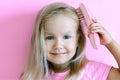 Little girl combing her hair. Beauty and childhood concept. Girl on a pink isolated background combing her hair with a pink comb Royalty Free Stock Photo