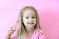 Little girl combing her hair. Beauty and childhood concept. Girl on a pink isolated background combing her hair with a pink comb Royalty Free Stock Photo