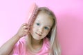 Little girl combing her hair. Beauty and childhood concept. Girl on a pink isolated background combing her hair with a pink comb Royalty Free Stock Photo