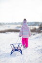 A little girl comes down from a snow slide and pulls a sled