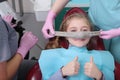 A little girl is comfortable to treat her teeth under superficial sedation. The girl smiles and holds two thumbs up. Milk teeth