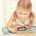 Little girl considering a world map with a magnifying glass