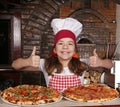 Little girl cook with pizza and thumbs up in pizzeria Royalty Free Stock Photo