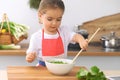 Little girl cooking in the kitchen. Kid slicing and mixing tomatoes and greenery. Concept of healthy meal or tasty Royalty Free Stock Photo