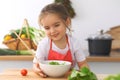 Little girl cooking in the kitchen. Kid slicing and mixing tomatoes and greenery. Concept of healthy meal or tasty Royalty Free Stock Photo