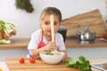 Little girl cooking in the kitchen. Kid slicing and mixing tomatoes and greenery. Concept of healthy meal or tasty Royalty Free Stock Photo