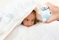 Little girl covering head with pillow and looking at alarm clock Royalty Free Stock Photo