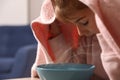 Little girl covering head with towel and inhaling steam indoors, closeup