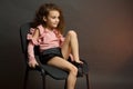 A little girl with curls in pink blouse and black shorts, sitting on an office chair with legs Studio portrait Royalty Free Stock Photo