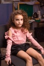 A little girl with curls in a pink blouse and black shorts is sitting on an office chair Royalty Free Stock Photo