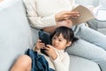 Little girl is cute lying next to the cell phone playing Pregnant Asian single mom Sit comfortably on the sofa in the living room