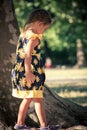 Little girl in cute summer dress walk in park by huge tree