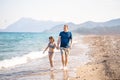 Little girl, dad, father walking on beach, sea ocean shore in sun protection swimsuit. Playing in sand, blue waves Royalty Free Stock Photo