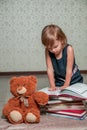 little girl in dark blue dress reading book sitting on the floor near teddy bear. Child reads story for toy. Royalty Free Stock Photo