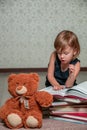 little girl in dark blue dress reading book sitting on the floor near teddy bear. Child reads story for toy. Royalty Free Stock Photo