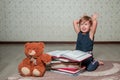 little girl in dark blue dress reading book sitting on the floor near teddy bear. Child reads story for toy. Showing bunny ears. Royalty Free Stock Photo