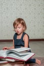 Little girl in dark blue dress reading book sitting on the floor near teddy bear. Child reads story for toy. Turns the page. Royalty Free Stock Photo