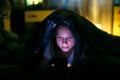 Little girl at dark looks at smartphone under a blanket in bed. Royalty Free Stock Photo