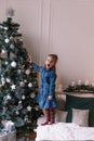 A little girl decorates the Christmas tree with toys and trinkets. Cute baby is getting ready to go home to celebrate Royalty Free Stock Photo