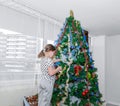 Little girl decorating big christmass tree in grey room