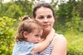 Little girl in a denim dress in the arms of her serious mother looking into the distance