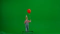 A little girl in denim overalls with a festive cap on her head and carrying a red helium balloon walks in front of a Royalty Free Stock Photo