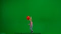 A little girl in denim overalls with a festive cap on her head and carrying a red helium balloon walks in front of a Royalty Free Stock Photo