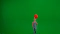 A little girl in denim overalls with a festive cap on her head and carrying a red helium balloon walks in front of a Royalty Free Stock Photo