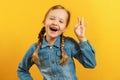 Little girl in a denim shirt on a yellow background. The child shows an OK sign. The concept of success, approval