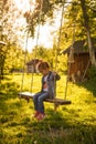 A little girl in a denim suit swings on a suspended swing to a tree. Royalty Free Stock Photo