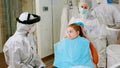 Little girl with dental bib and ppe suit listening pediatric dentist in coverall Royalty Free Stock Photo