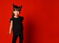 Little girl with devil horns, in black blouse and leggings posing against red studio background. Masquerade, Halloween. Close up Royalty Free Stock Photo