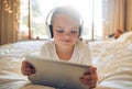 Little girl with digital tablet and headphones on the bed at home. Cute child looking happy while watching cartoons with Royalty Free Stock Photo