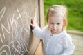 Little girl drawing on blackboard. Toddler girl having fun outdoors, holding chalk and drawing. Royalty Free Stock Photo