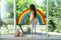 Girl drawing rainbow on window with paints indoors. Stay at home concept