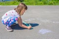 A little girl draws with crayons on the asphalt, on a sunny day Royalty Free Stock Photo