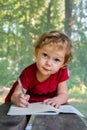 Little girl draws in a notebook on a background of nature. The beautiful, emotional face of a child of three years